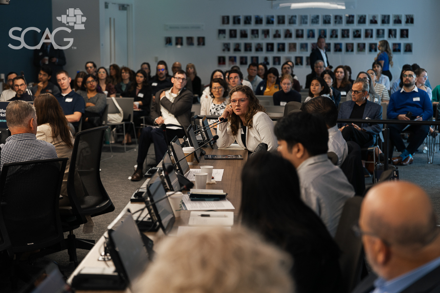 Meeting with diverse people seated at tables, discussing attentively in a brightly lit room.