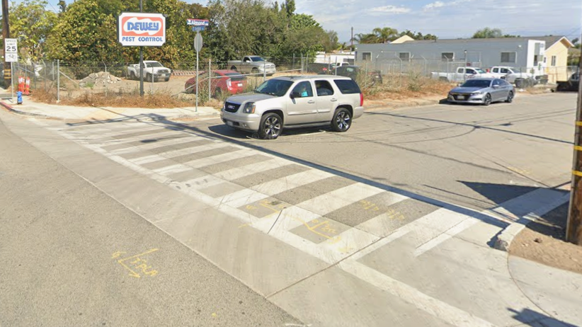 Intersection with a crosswalk, cars and distant buildings under a clear sky.