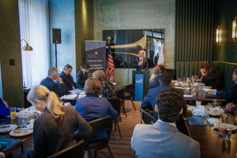 Business meeting with speaker at podium, attendees seated at tables.